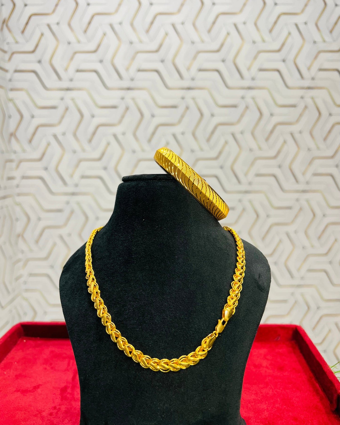 Gold necklace and bracelet on a black mannequin against a geometric patterned wall.